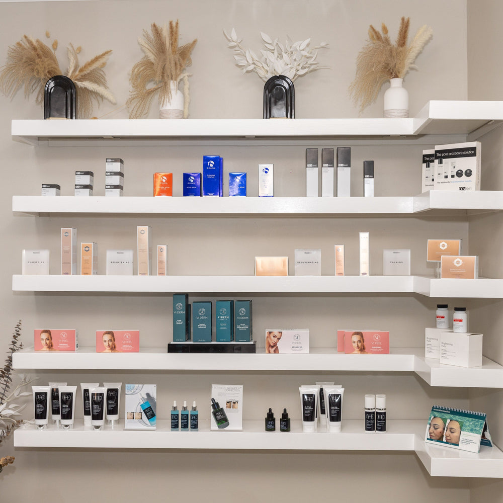 A wall-mounted white shelving unit displaying multiple skincare and beauty products in various packaging colors, set against a beige wall with decorative dried grass arrangements.